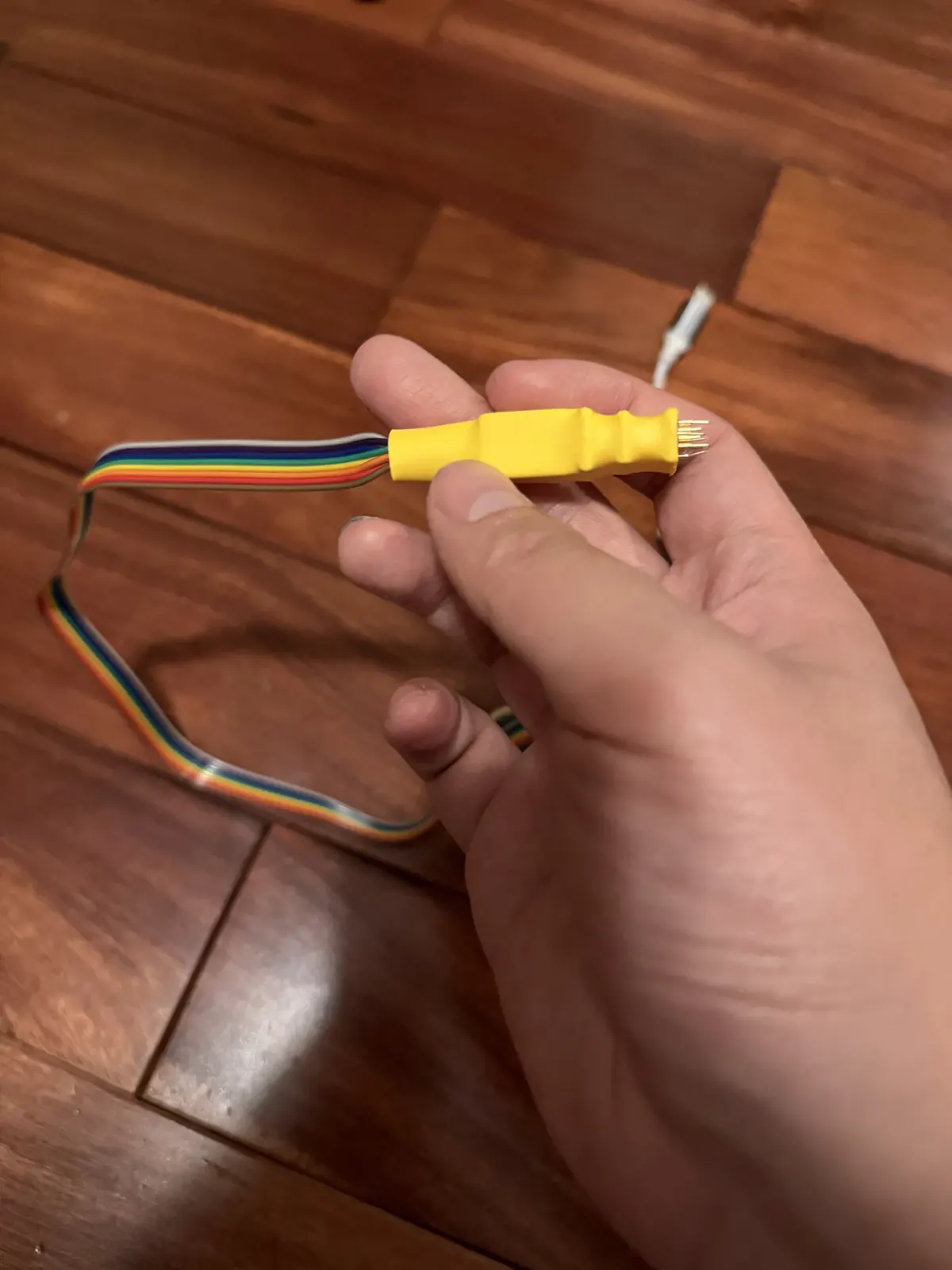 A hand pressing a yellow WSON8 pogo-pin probe, with a rainbow ribbon cable trailing off across a wood floor